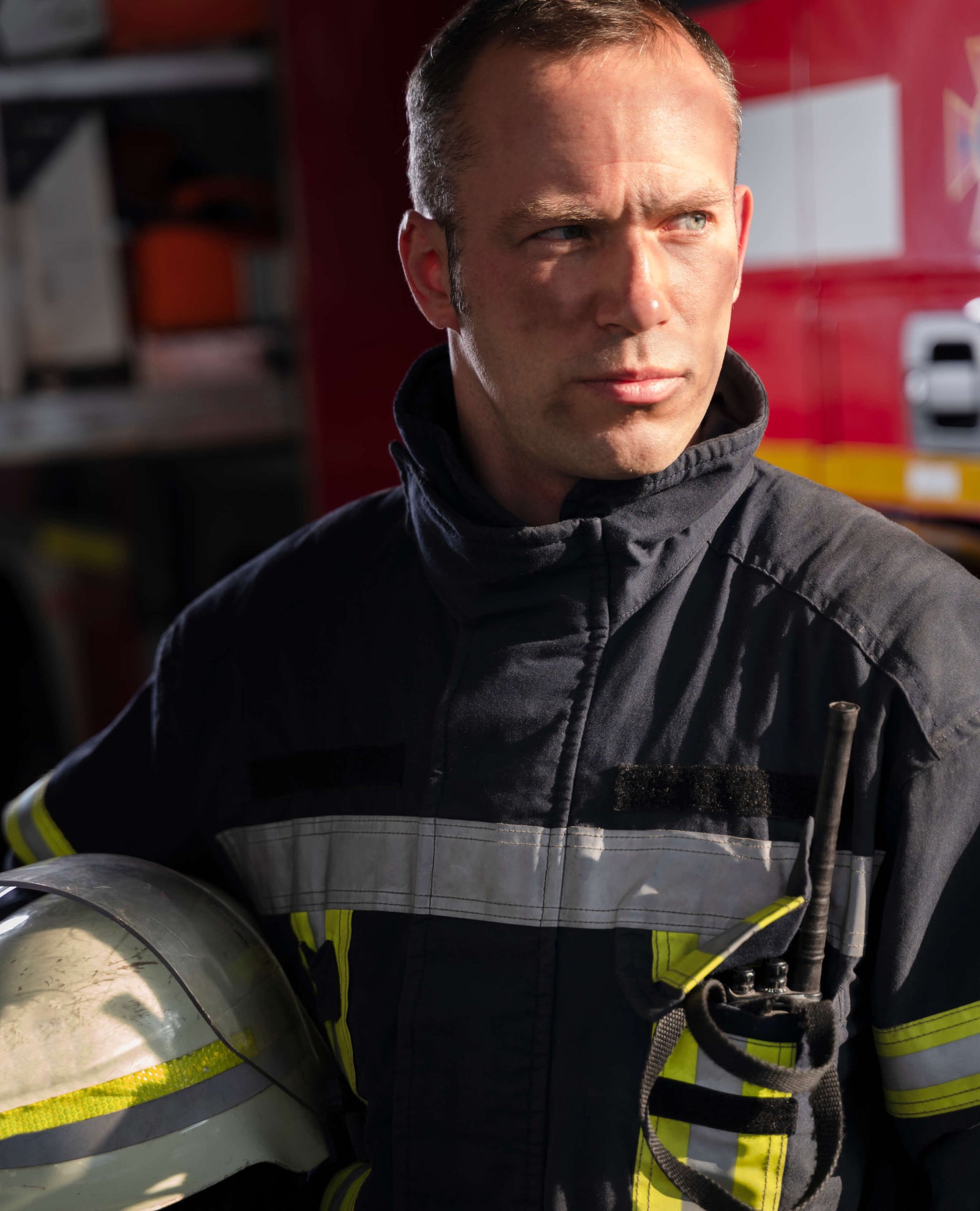 Firefighter holding a helmet with a fire truck in the background