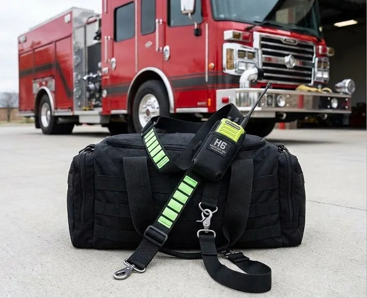H6 glow-in-the-dark radio strap with a yellow radio resting on a black gear bag in front of a red fire truck